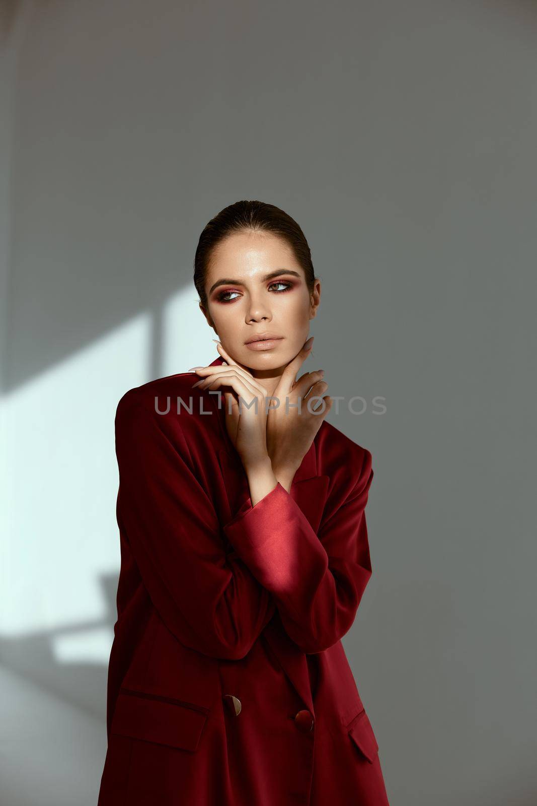 brunette with bright makeup holds hands near face glamor fashionable clothes red jacket. High quality photo