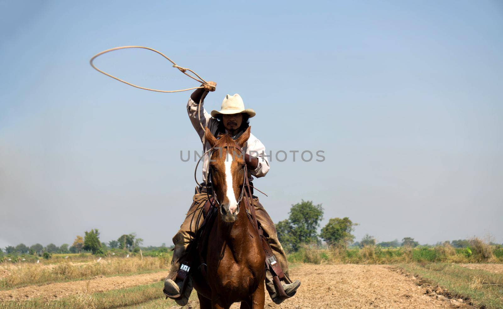 Rider as cowboy outfit costume with a horses and a gun held in the hand against smoke and sunset background