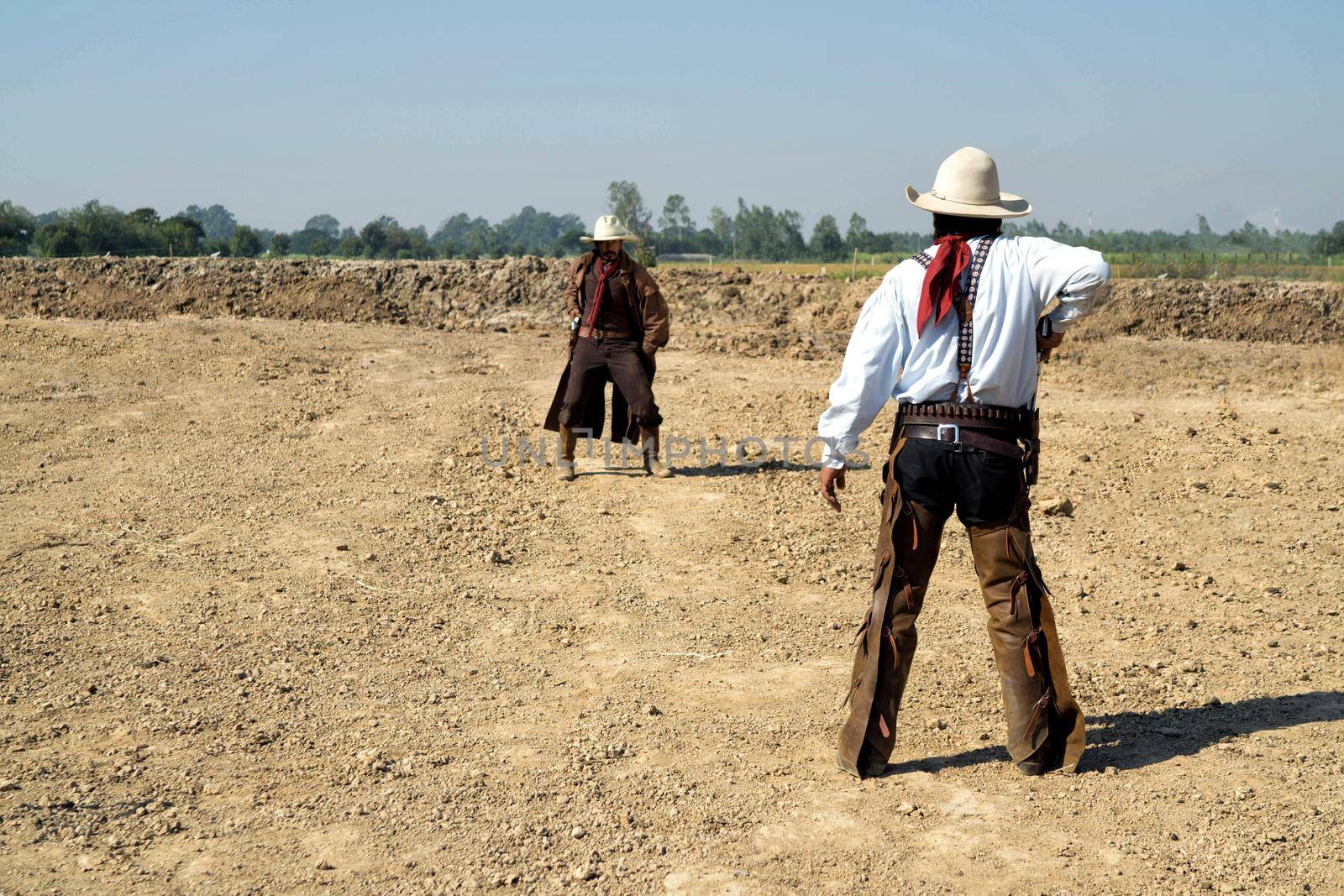 Two cowboy outfit costume with a gun held in the hand on gun fight against smoke and sun light on the buttle field. by chuanchai