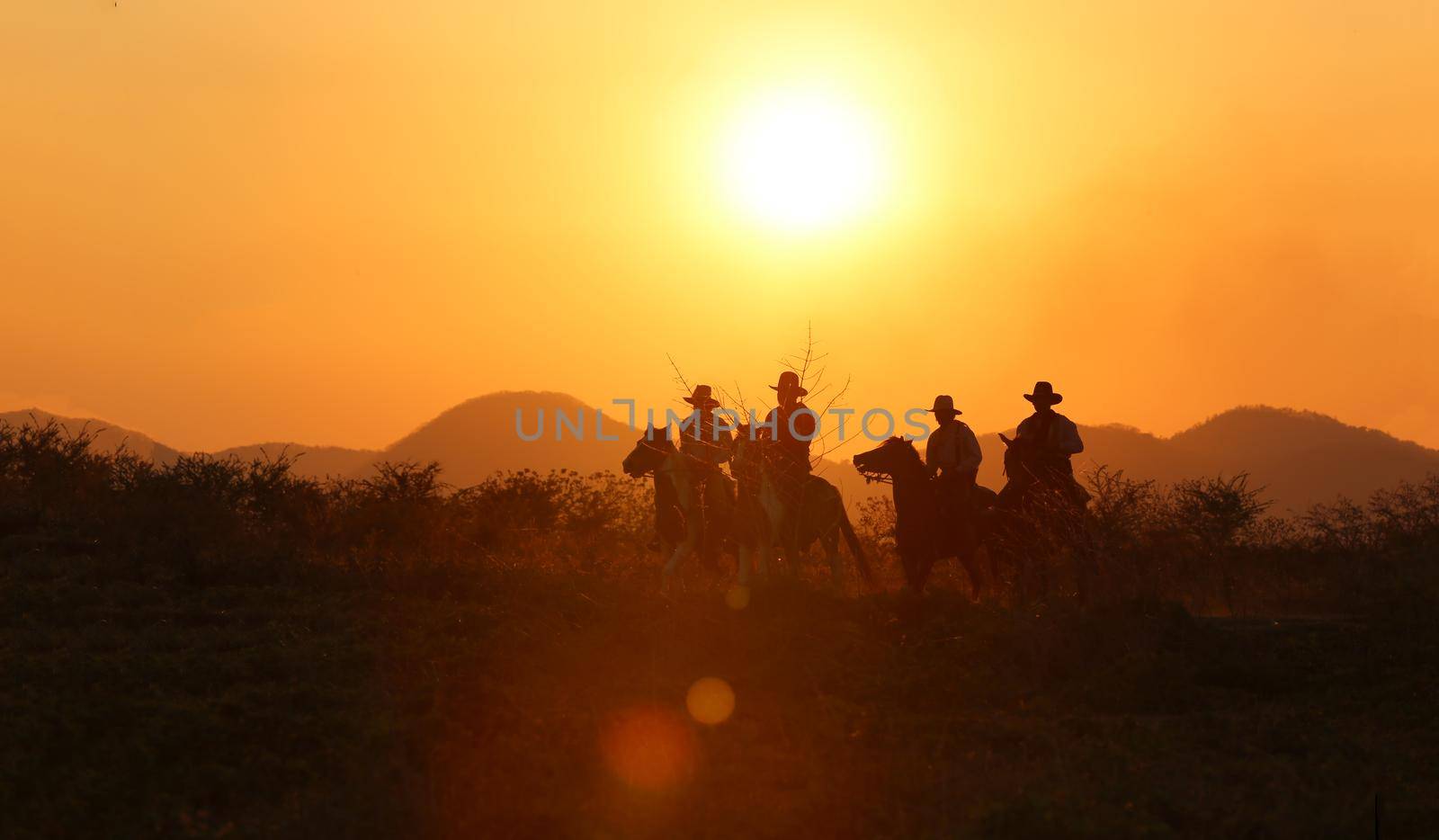 The silhouette of  rider as cowboy outfit costume with a horses and a gun held in the hand against smoke and sunset background