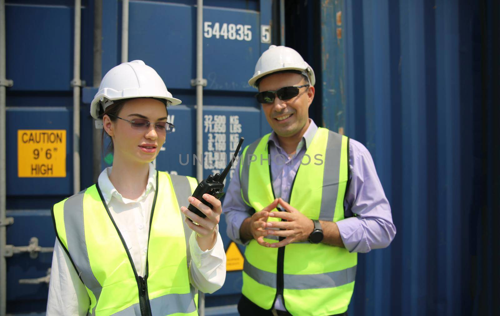 Manager and dock worker under discussion about dock container shipping warehouse document, they wearing safety uniform hard hat ,face mask and hold radio communication. by chuanchai
