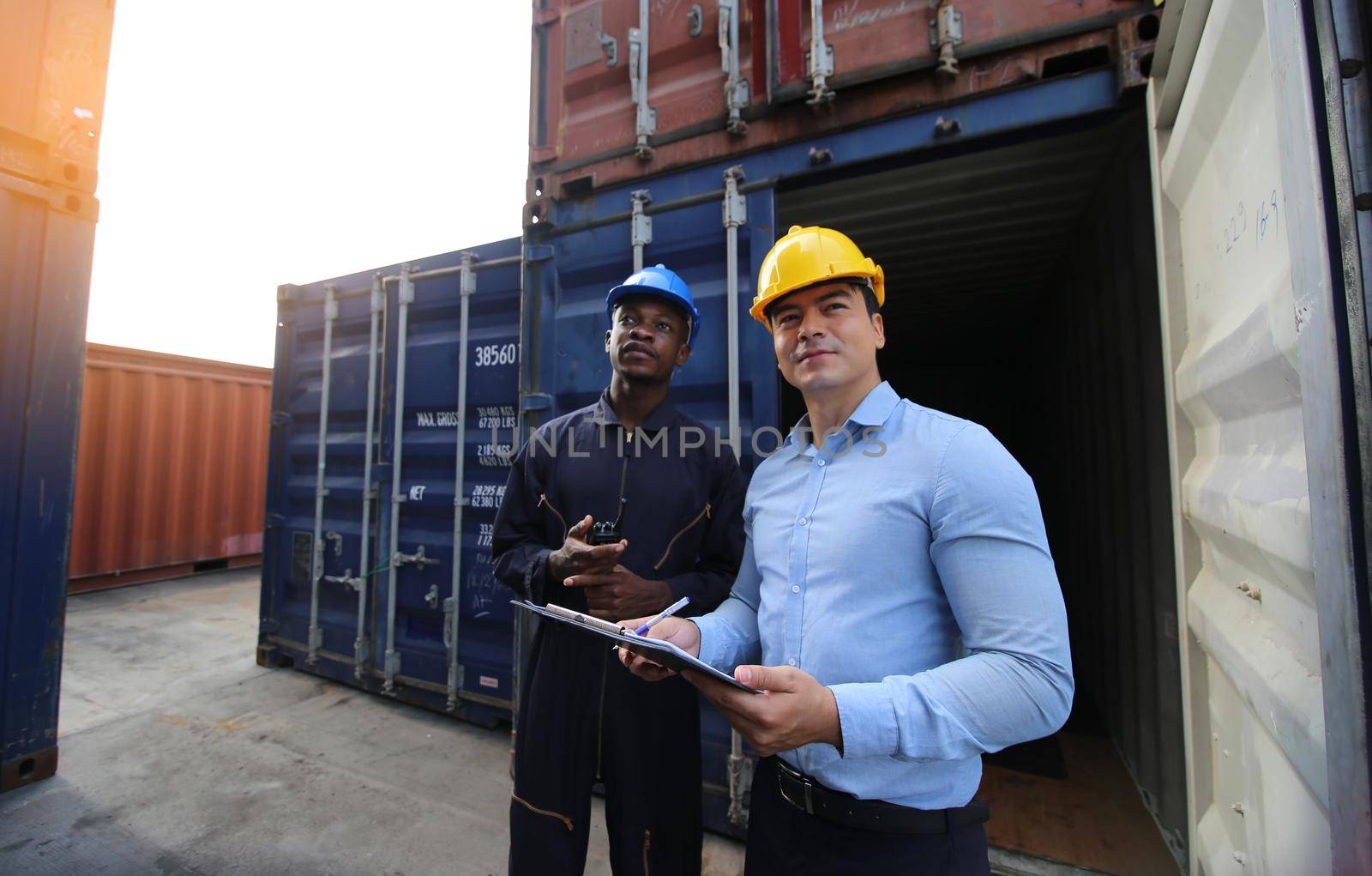 Manager and dock worker under discussion about dock container shipping warehouse document, they wearing safety uniform hard hat ,face mask and hold radio communication. by chuanchai