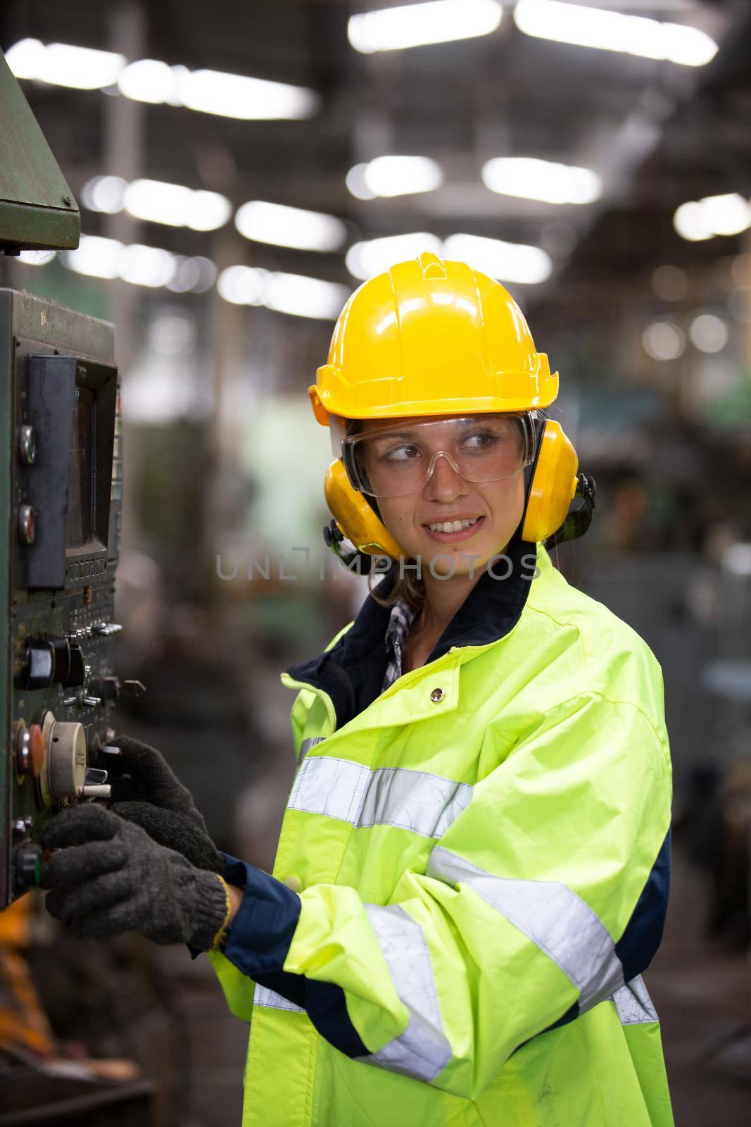 Woman worker wearing safety goggles control lathe machine to drill components. Metal lathe industrial manufacturing factory