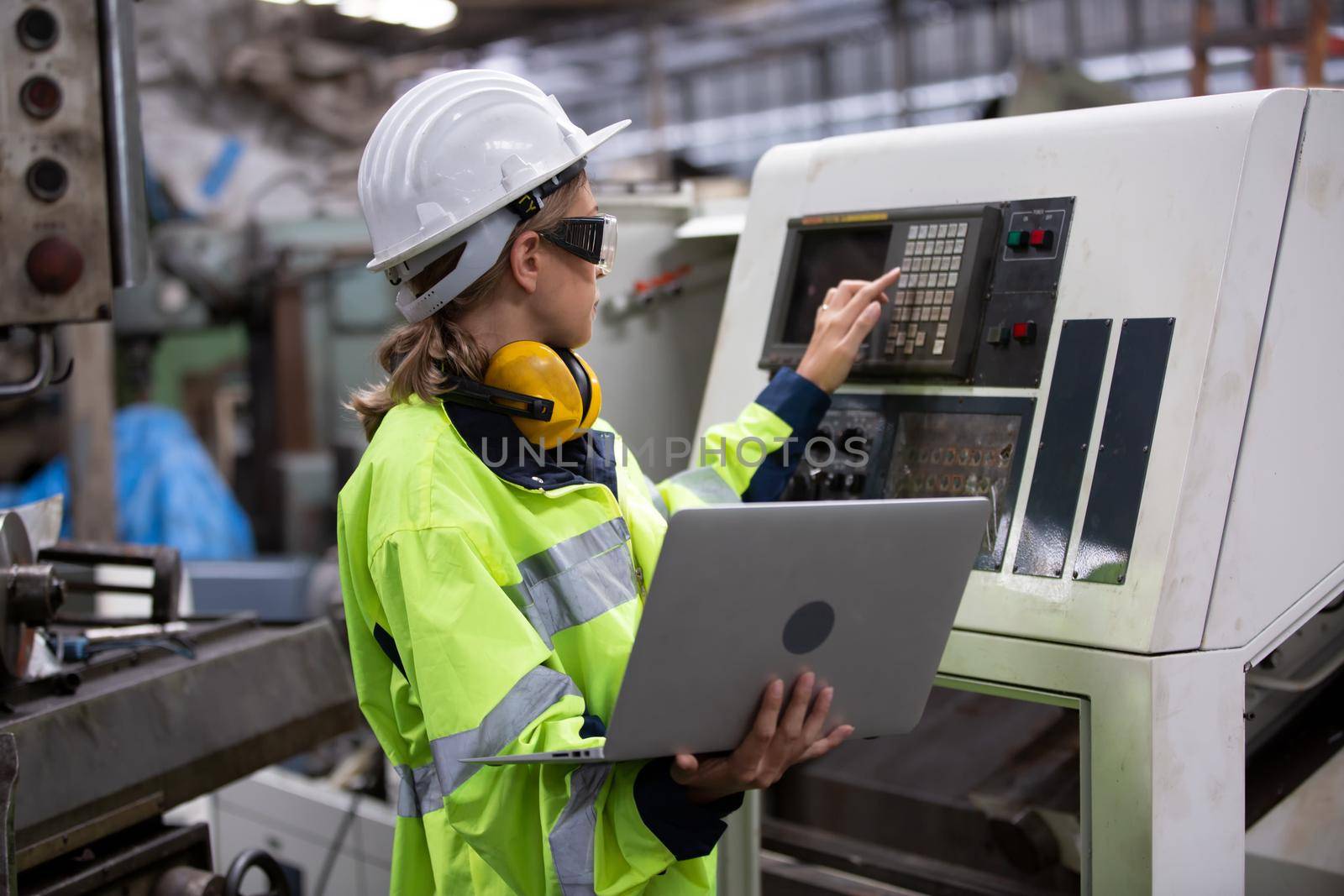 Woman worker wearing safety goggles control lathe machine to drill components. Metal lathe industrial manufacturing factory