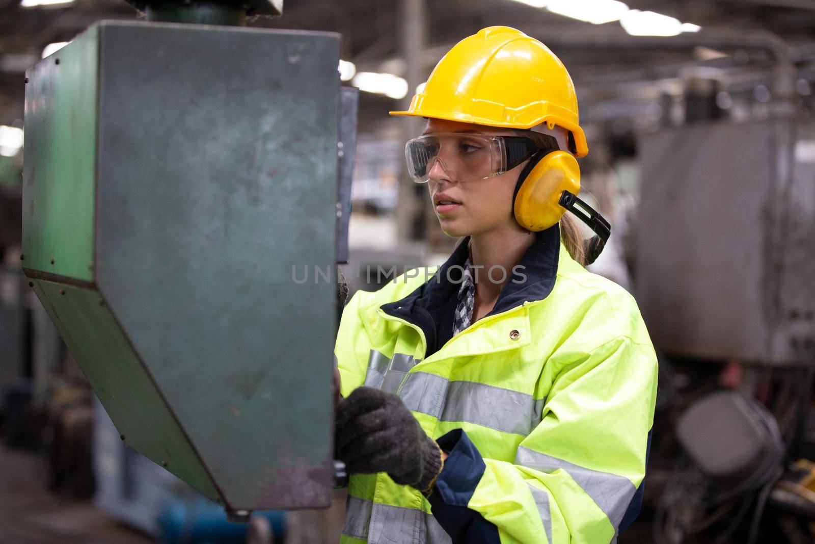 Woman worker wearing safety goggles control lathe machine to drill components. Metal lathe industrial manufacturing factory