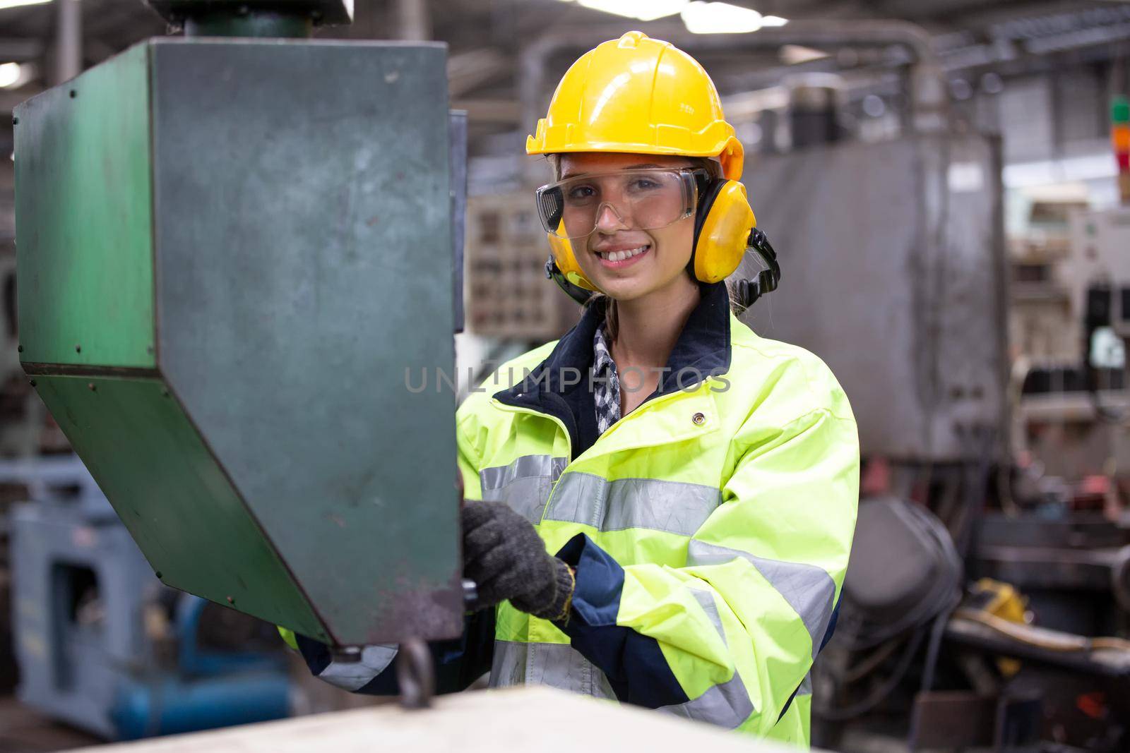 Woman worker wearing safety goggles control lathe machine to drill components. Metal lathe industrial manufacturing factory