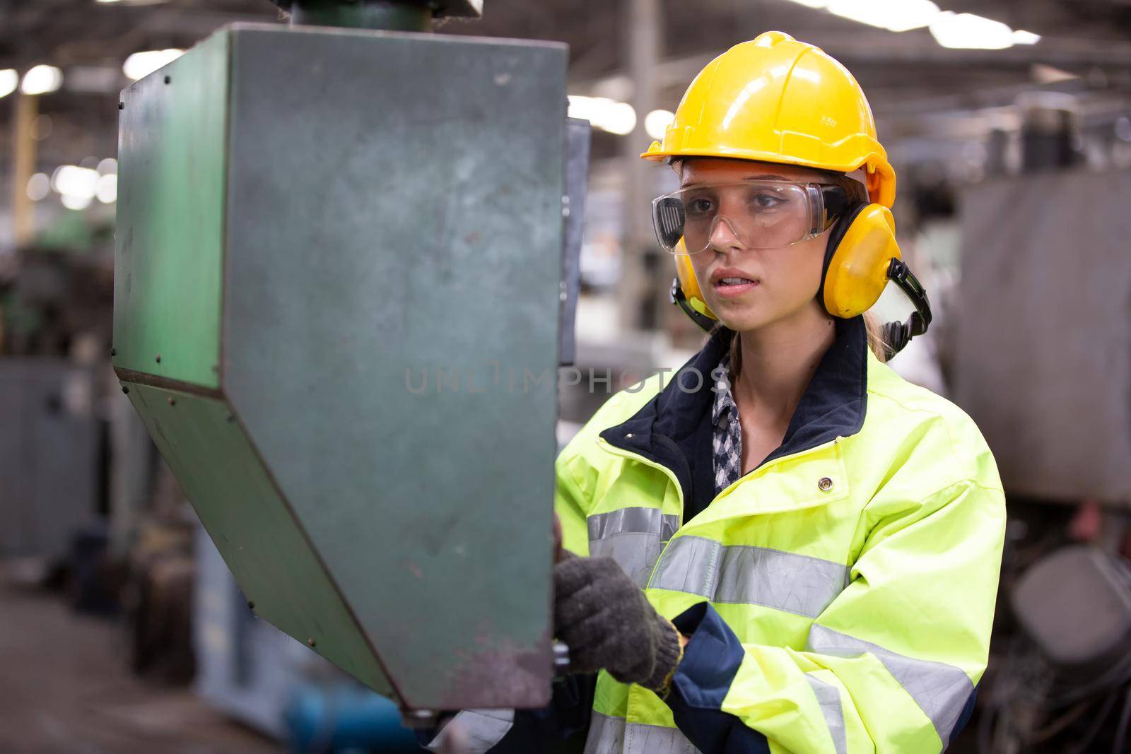Woman worker wearing safety goggles control lathe machine to drill components. Metal lathe industrial manufacturing factory