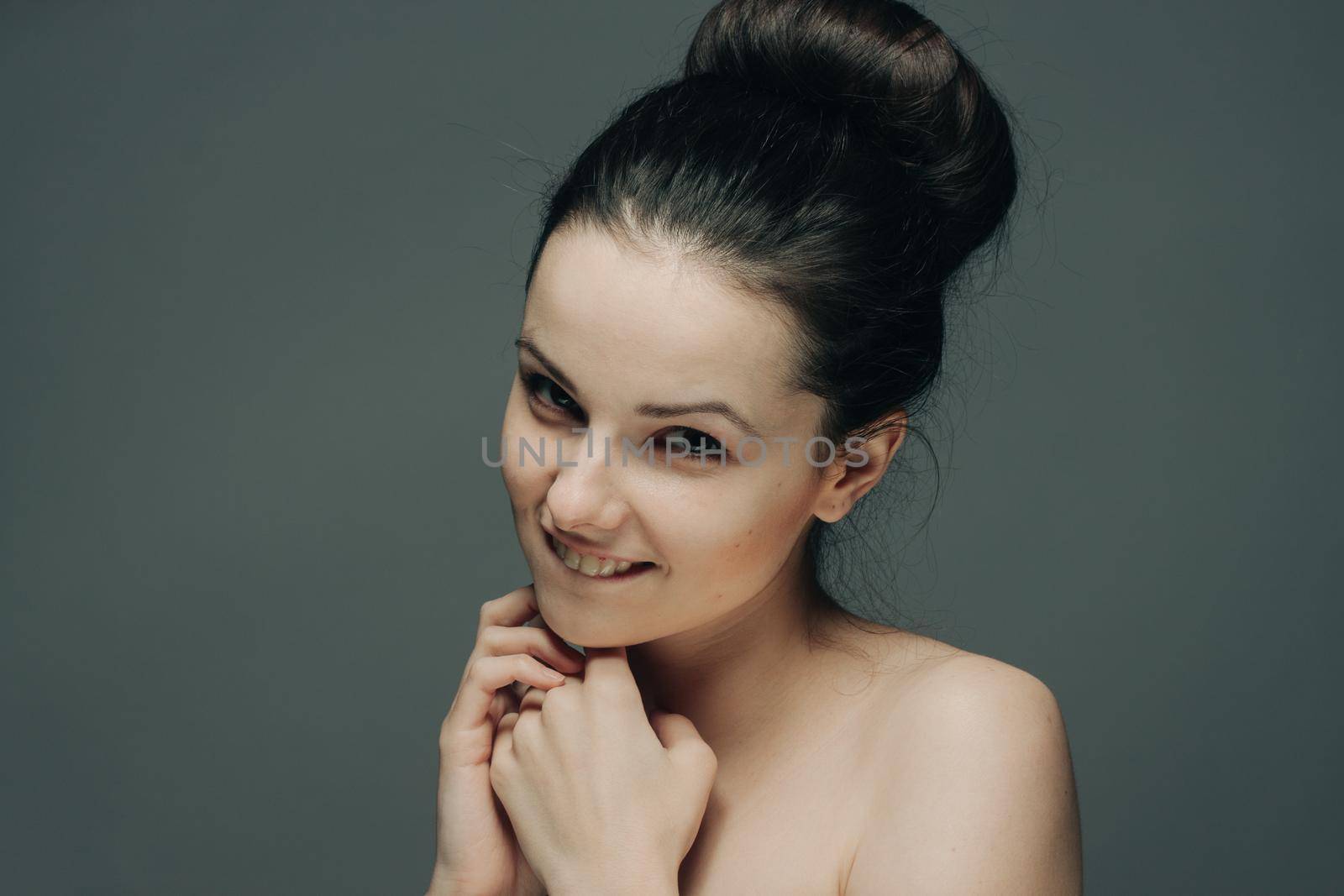 nude woman with hairstyles in her head touches her face with her hands on a gray background. High quality photo