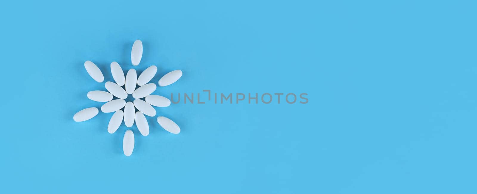 Flower shape made from white tablets on a blue backdrop with copy space.