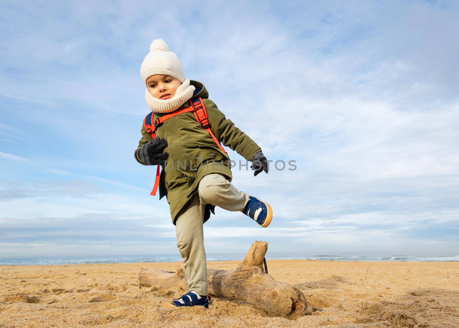 Little boy walking over a log on beach, winter season, low angle shot