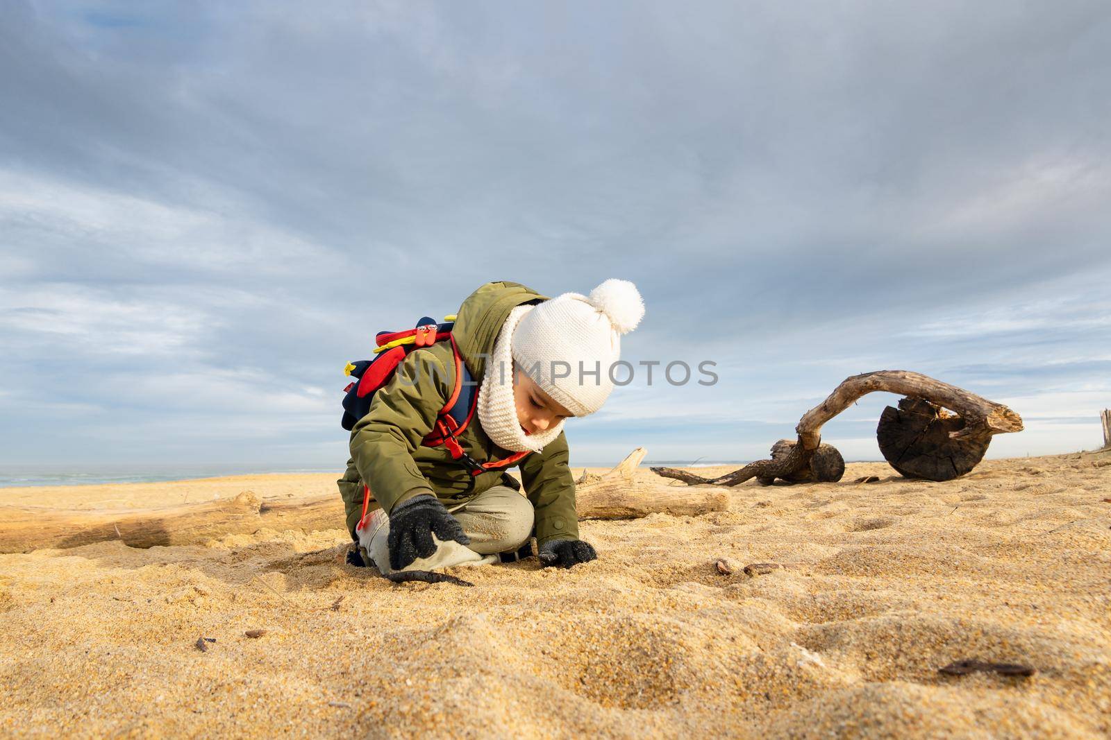 Little boy playing in the sand on beach in winter
