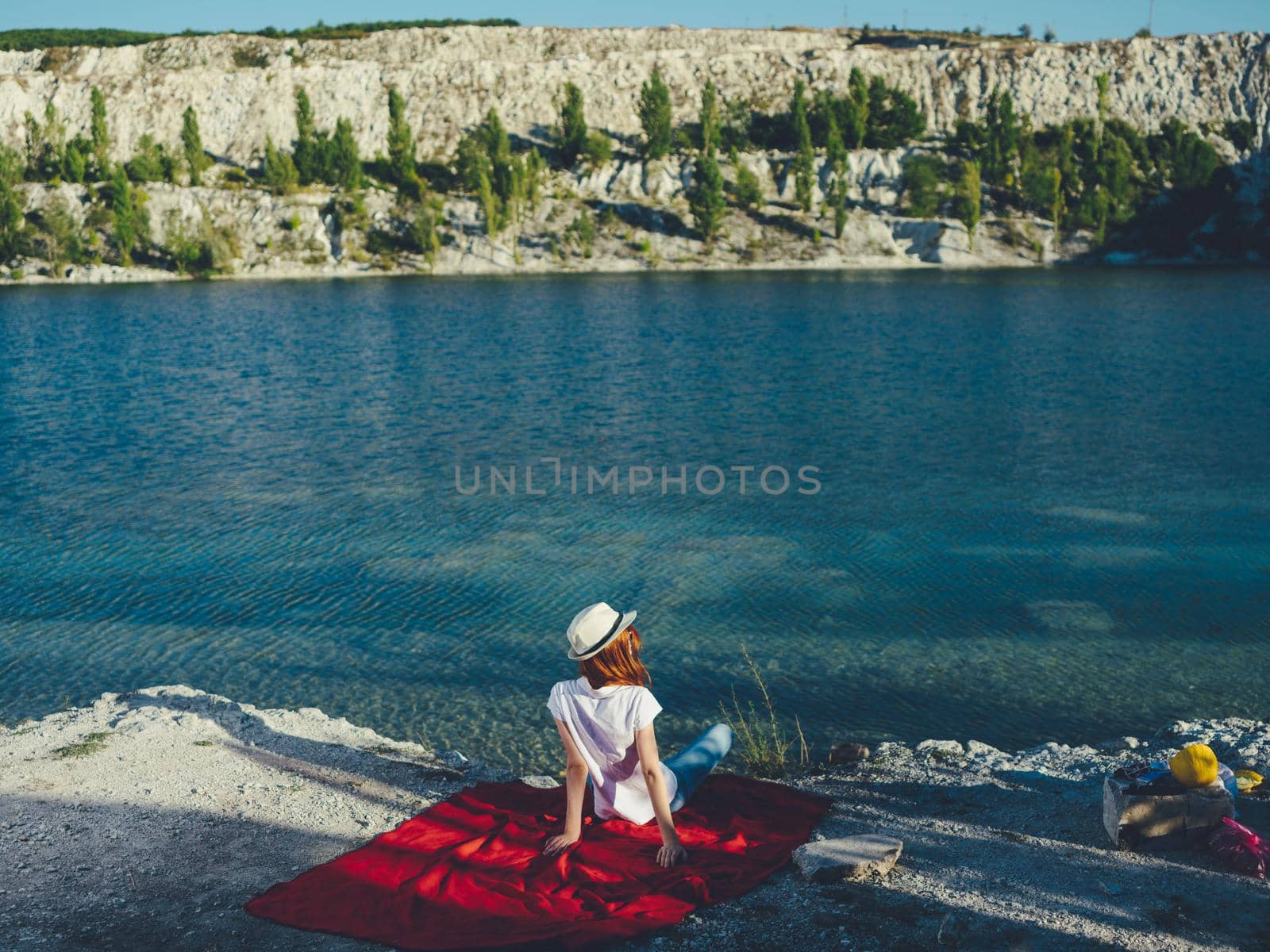 A woman sits on a red cloth near the river and a hat on her head by SHOTPRIME