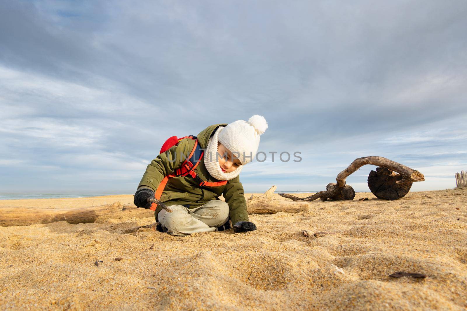 Little boy playing in the sand on beach in winter