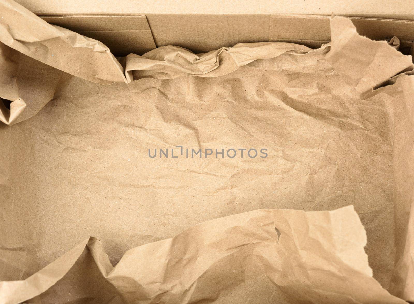 open empty rectangular brown cardboard box for transportation and packaging of goods, top view. At the bottom is a piece of brown paper