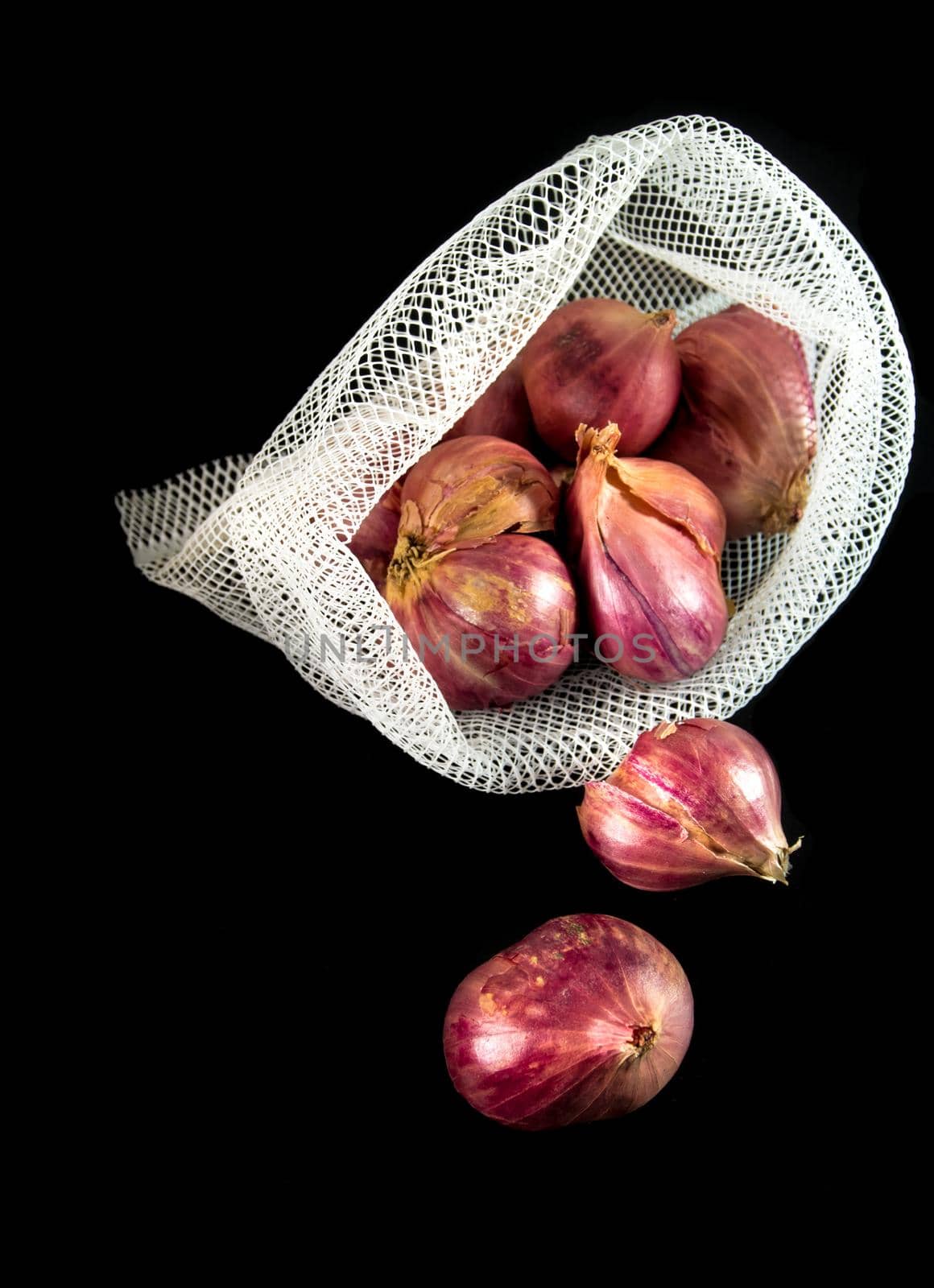 Red onions in mesh bag and some on floor isolated on black background by Satakorn