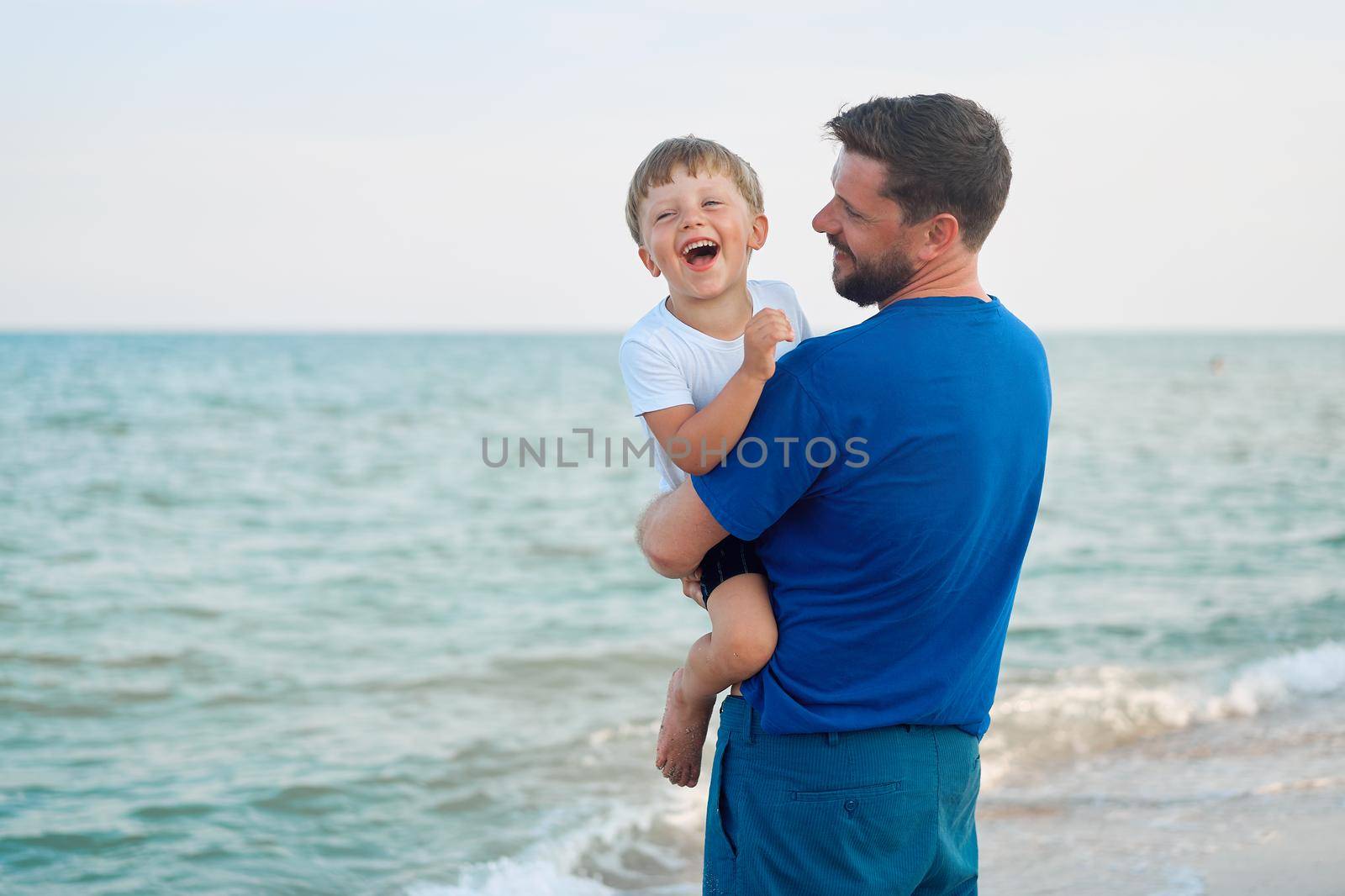 Father son spending time together sea vacation Young dad child little boy walking beach Fathers day. Family with one child. Happy childhood with daddy. sitting on hands laughs