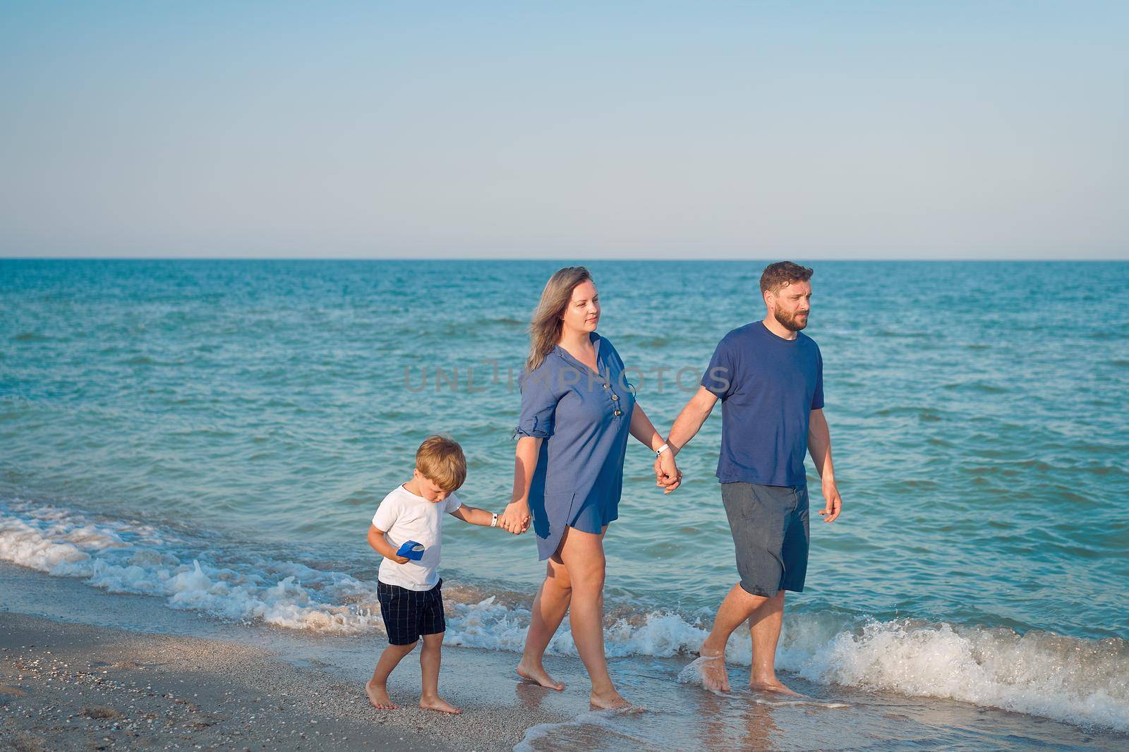 Mother father kid spending time together family vacation Parent dad mom walking with son holds hand barefoot on sea water enjoying summer holidy Happy family concept. Blue color clothes. Full lenght