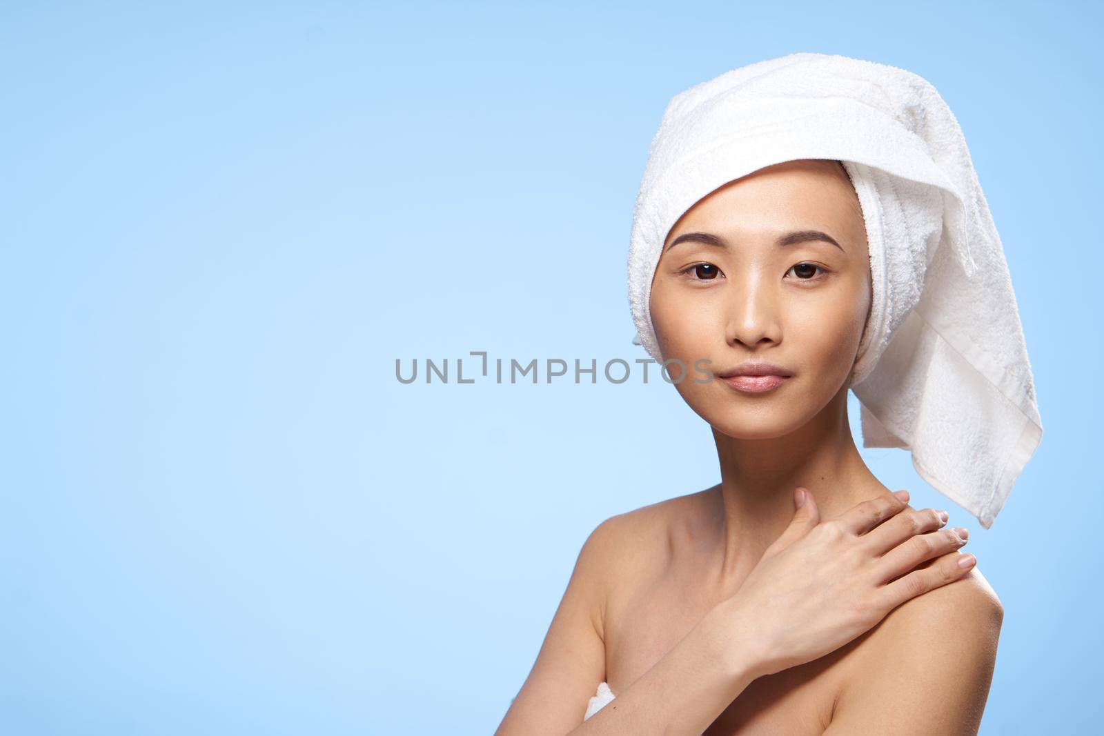pretty woman asian appearance bare shoulders towel on head spa procedure blue background. High quality photo