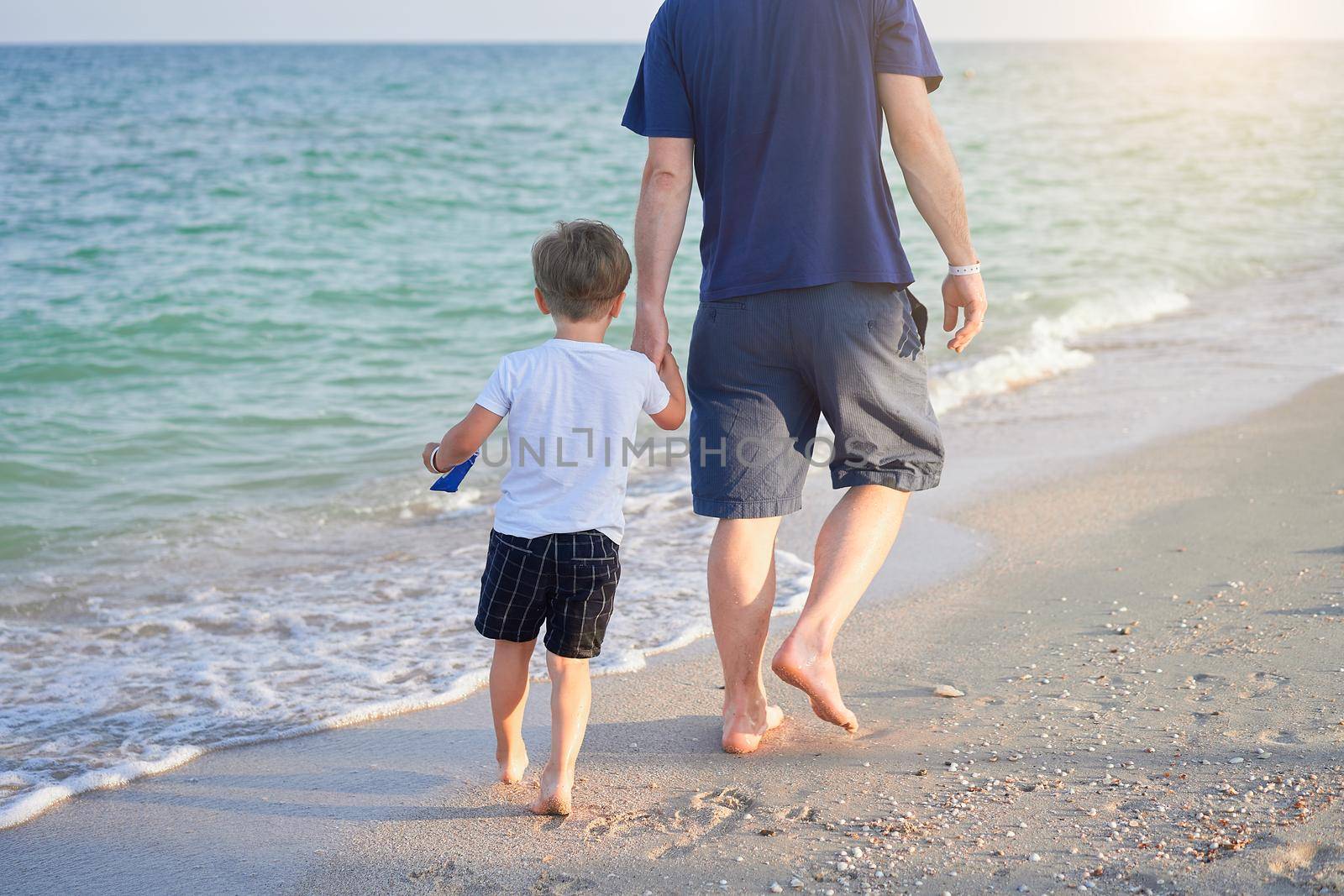 Dad holds son hand. Father Child spending time together sea vacation Young man little boy walking beach Fathers day. Family with one child. Happy childhood with daddy.