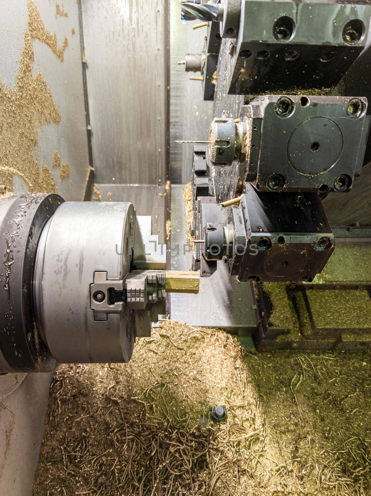 cnc lathe with lot of brass swarf inside while turning hexagonal yellow metal rod workpiece.