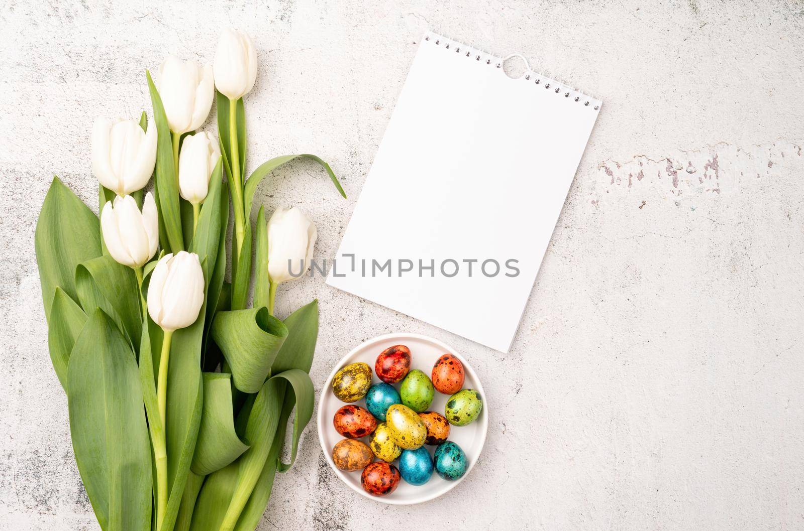 Top view of white tulips, blank calendar and colored easter eggs on concrete backgrund with copy space by Desperada