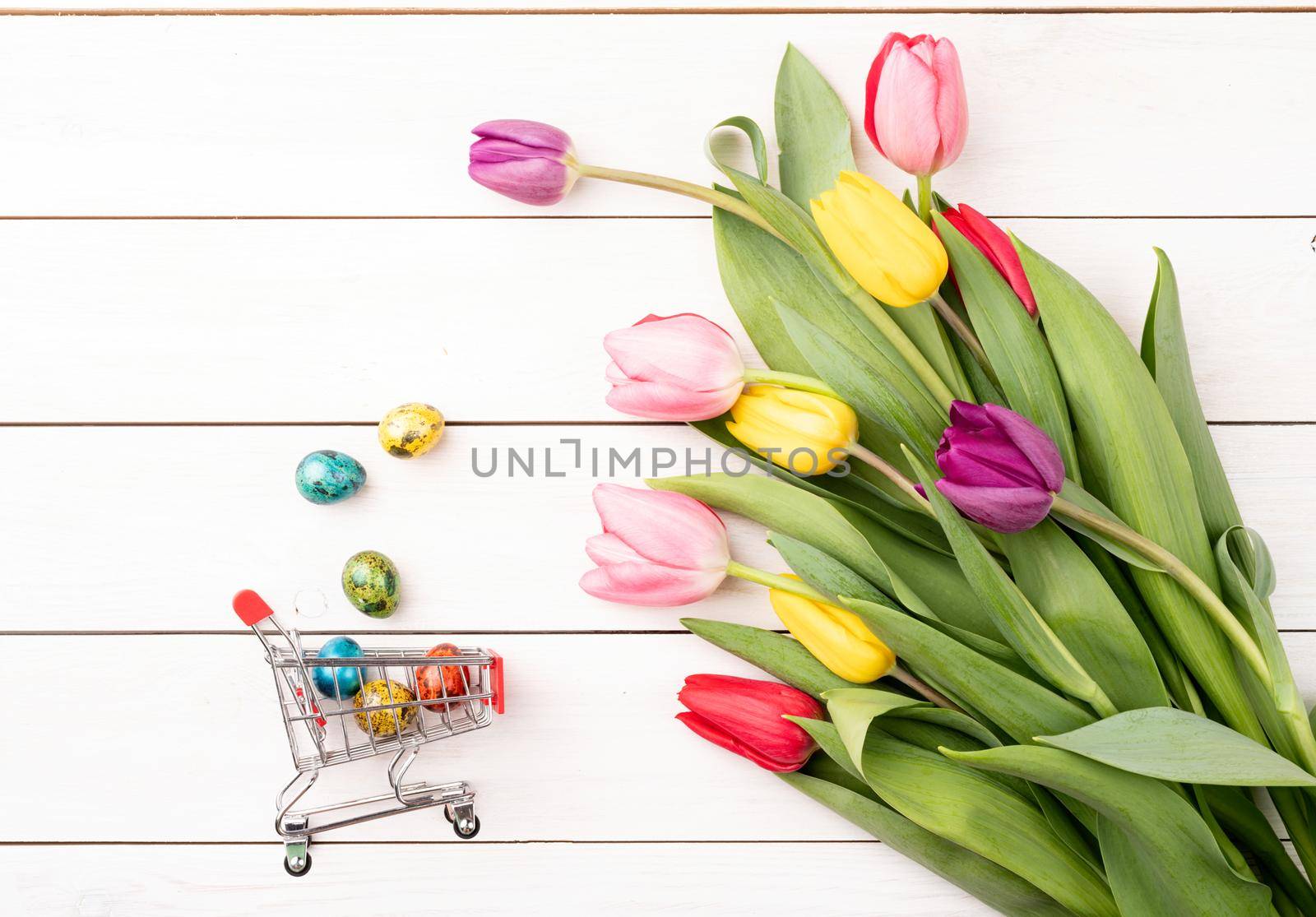 Holiday shopping. Shopping cart with colorful bouquet of tulips on white wooden background