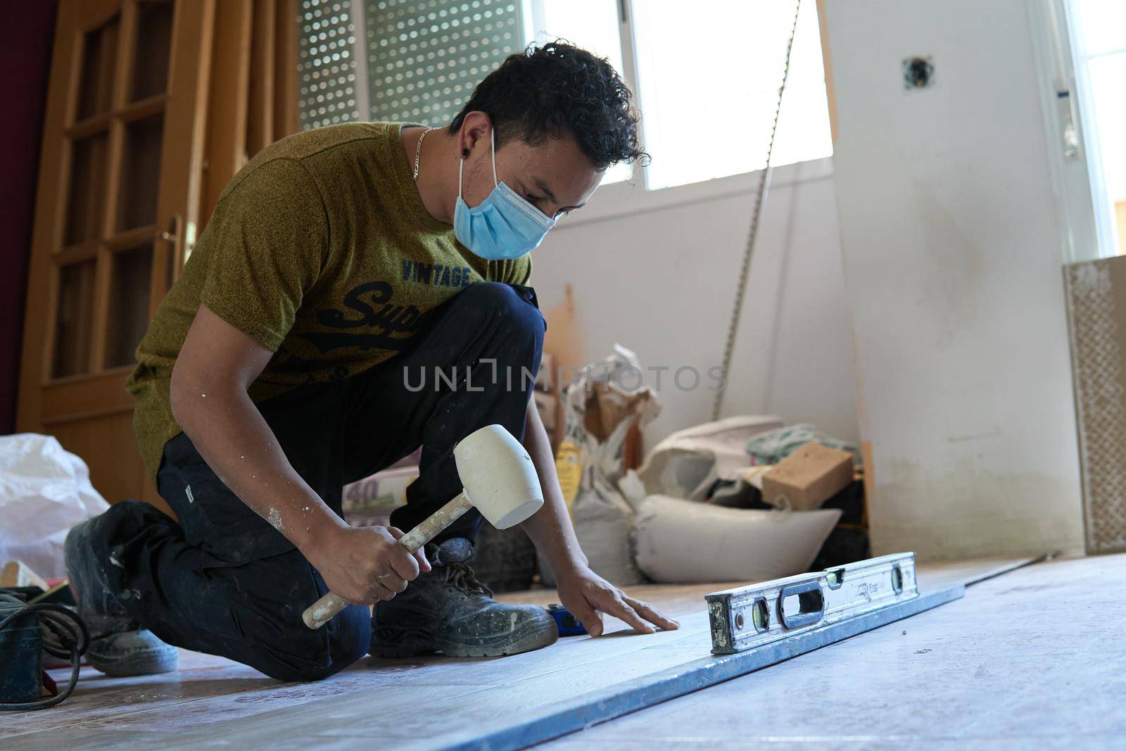 Mason tiling a room with a mustard-colored t-shirt and rubber pot and level and with a mask