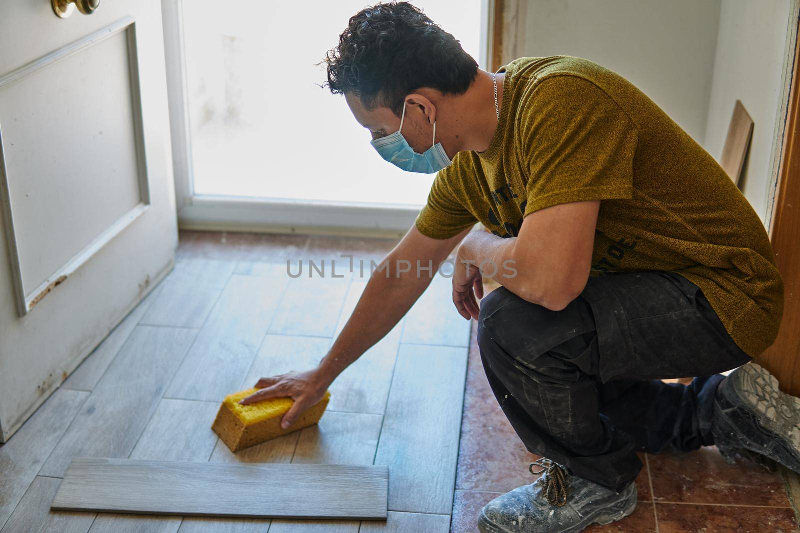 Worker cleaning the floor with a sponge and protective mask next to a door