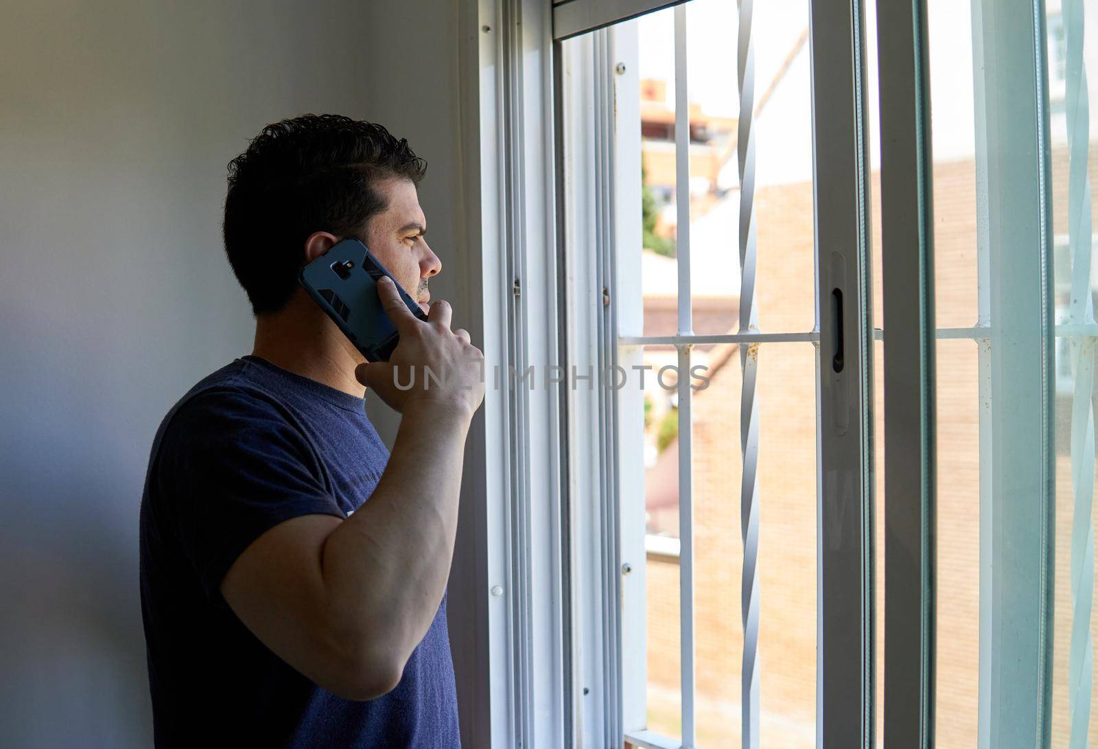 Man talking on a cell phone in a room next to a window