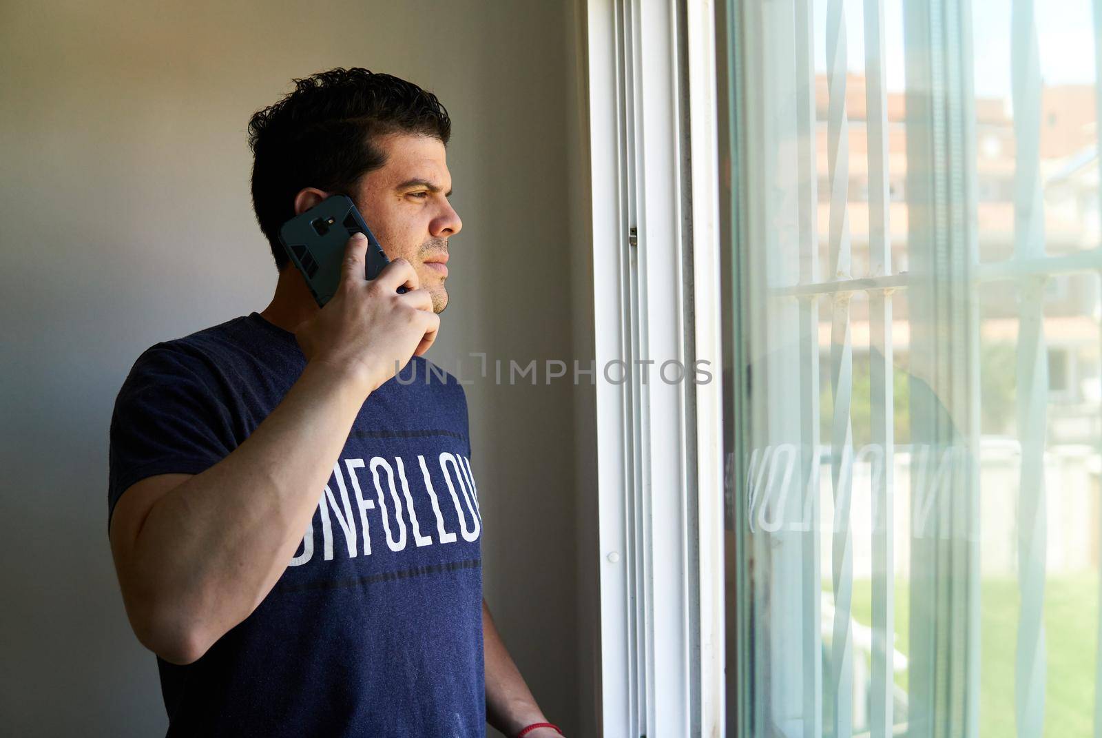 Man talking on a cell phone in a room next to a window