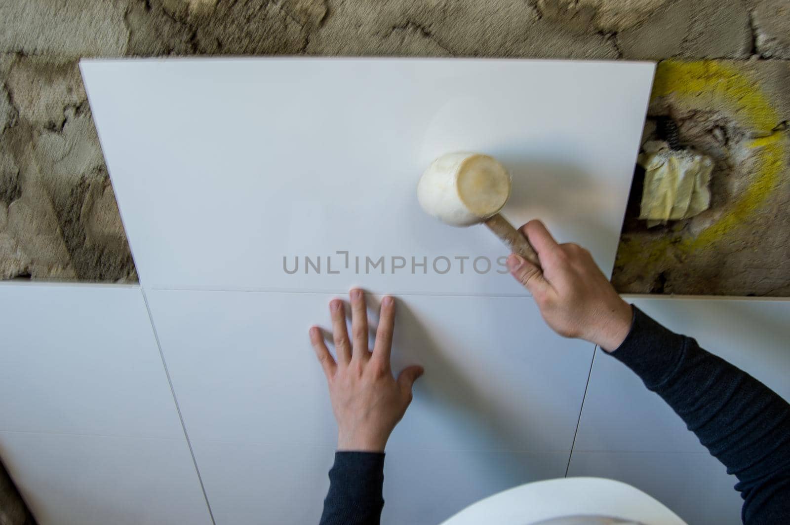 Bricklayer tiling a wall with white tiles and a rubber pot