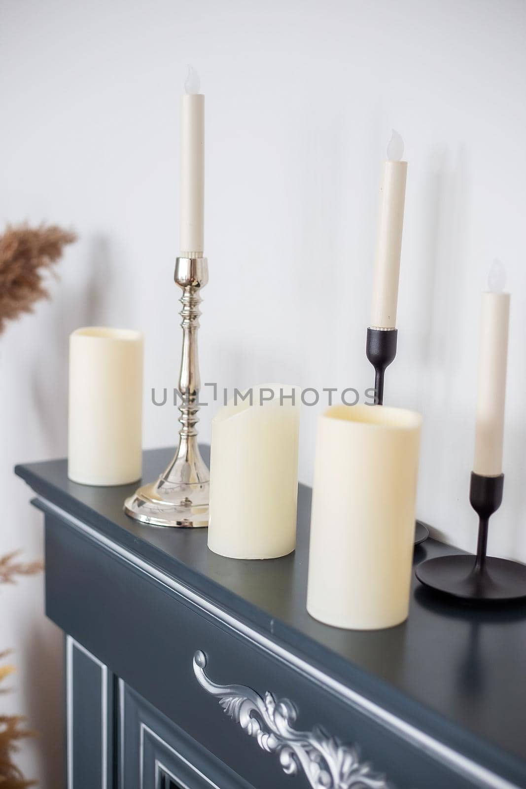 Candles of various types and sizes with and without candlesticks on the imitation fireplace countertop near the wall