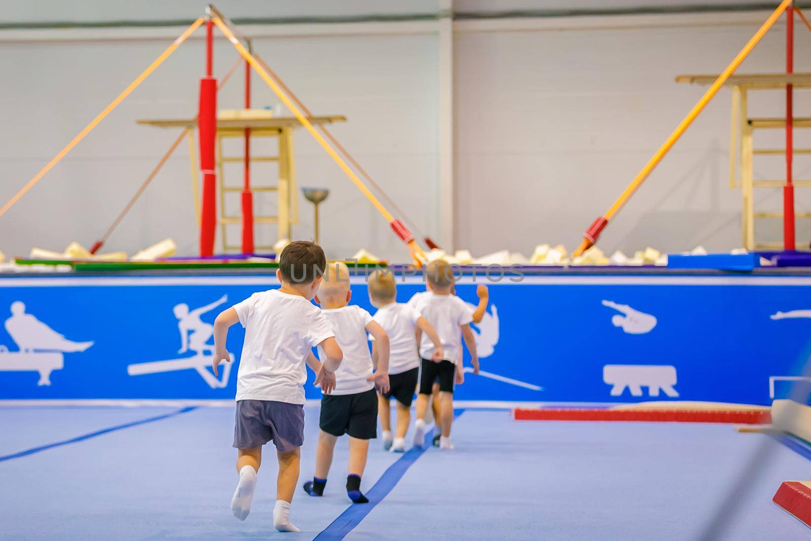 Small children, boys in training run in a circle in the hall under the guidance of a coach. Gymnastics.