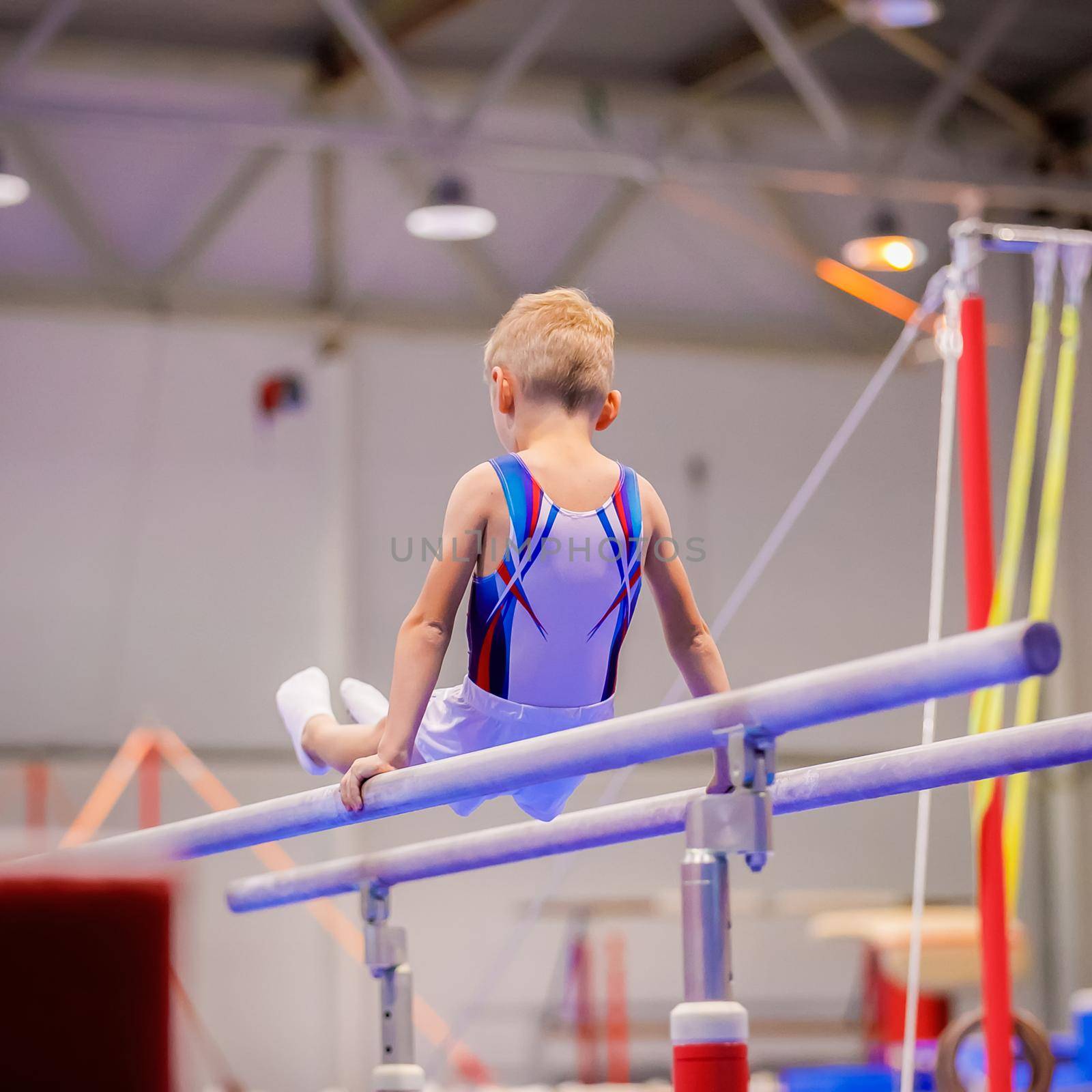 A little boy in sportswear performs an exercise on the uneven bars. Rhythmic gymnastics, training in the hall.