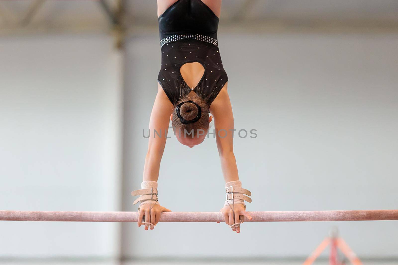 A girl in sportswear performs an exercise on the uneven bars. Rhythmic gymnastics, training in the hall.