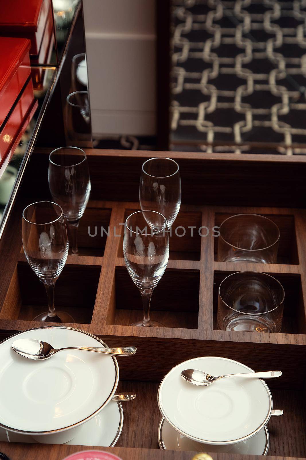 Pull-out drawer filled with glass wine glasses, cups, saucers and spoons.