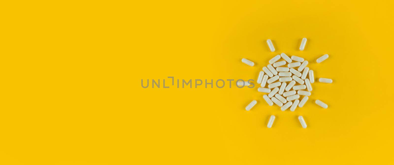 Sun shape made from white pills capsules on a yellow backdrop with copy space.