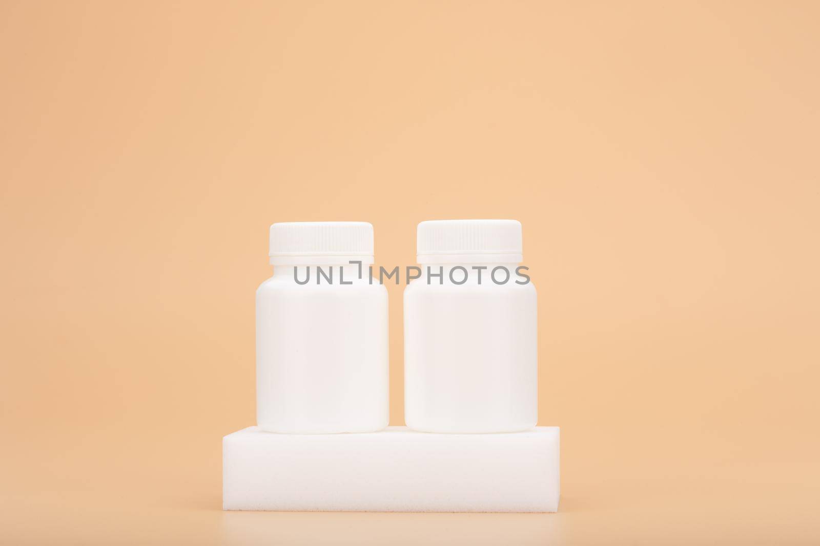 Two white medication unbranded bottles on white podium against beige background. Concept of vitamins, supplements, healthy lifestyle and wellbeing