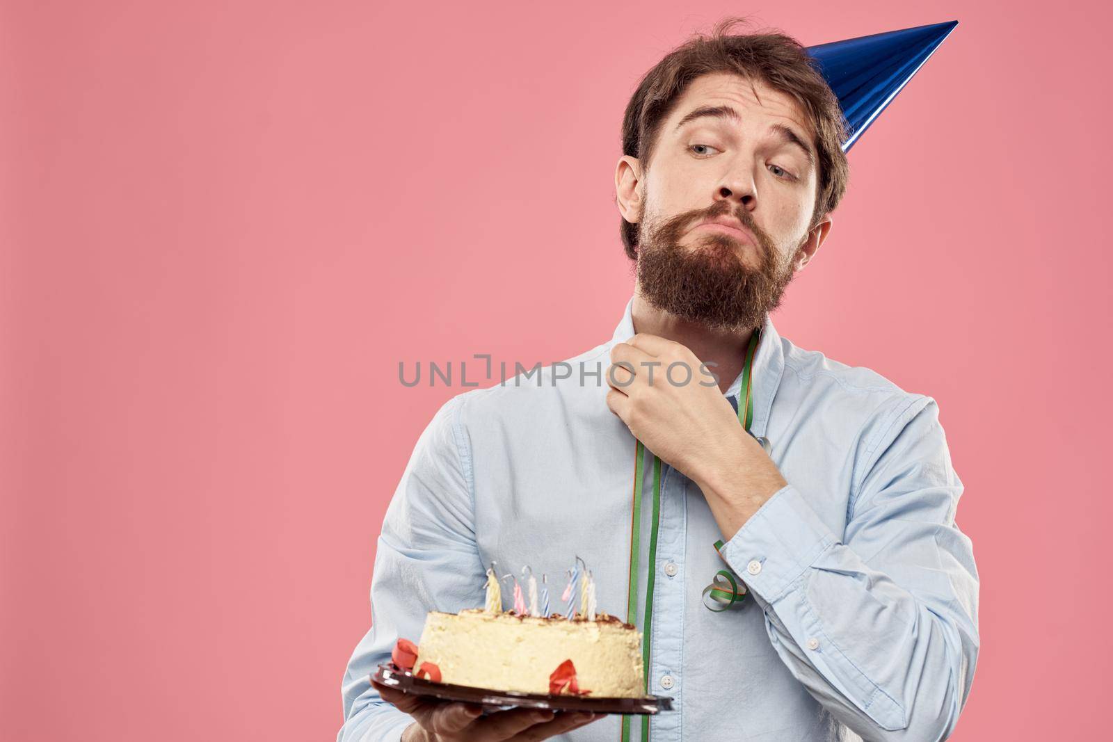 Bearded man with cake tongue on a pink background cropped view and a blue cap on his head. High quality photo
