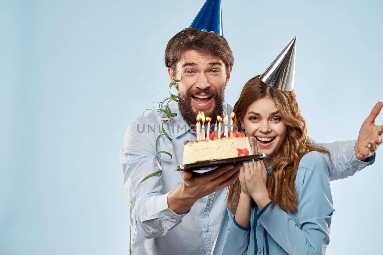 man and woman celebrate birthday with cake and in hats on blue background. High quality photo