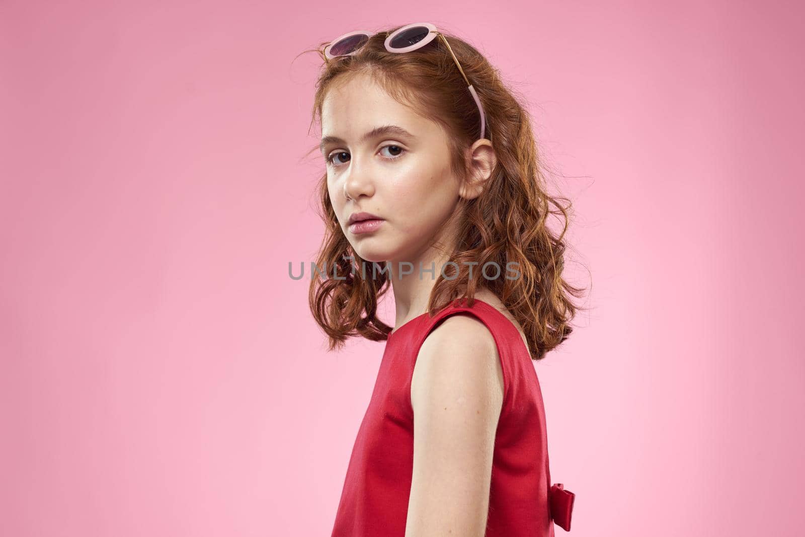 Cheerful little girl childhood dark glasses red dress lifestyle pink background. High quality photo