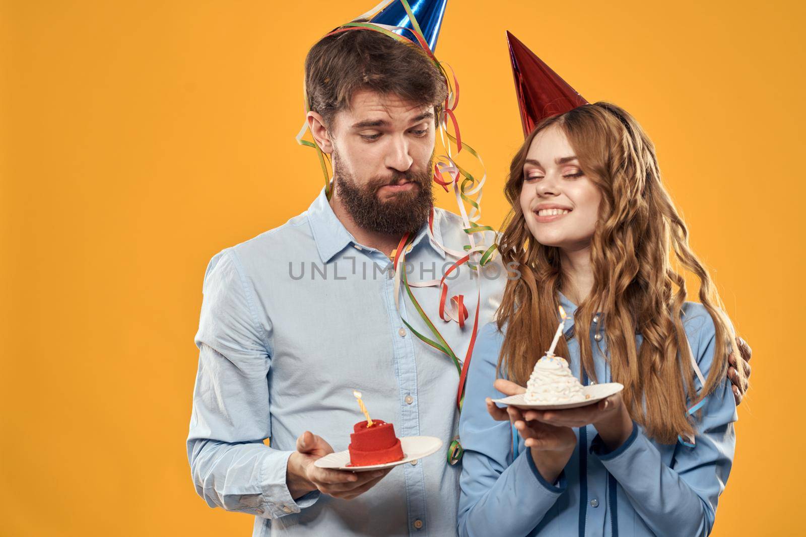 Energetic man and pretty woman with birthday cake in hats on a yellow background disco party. High quality photo
