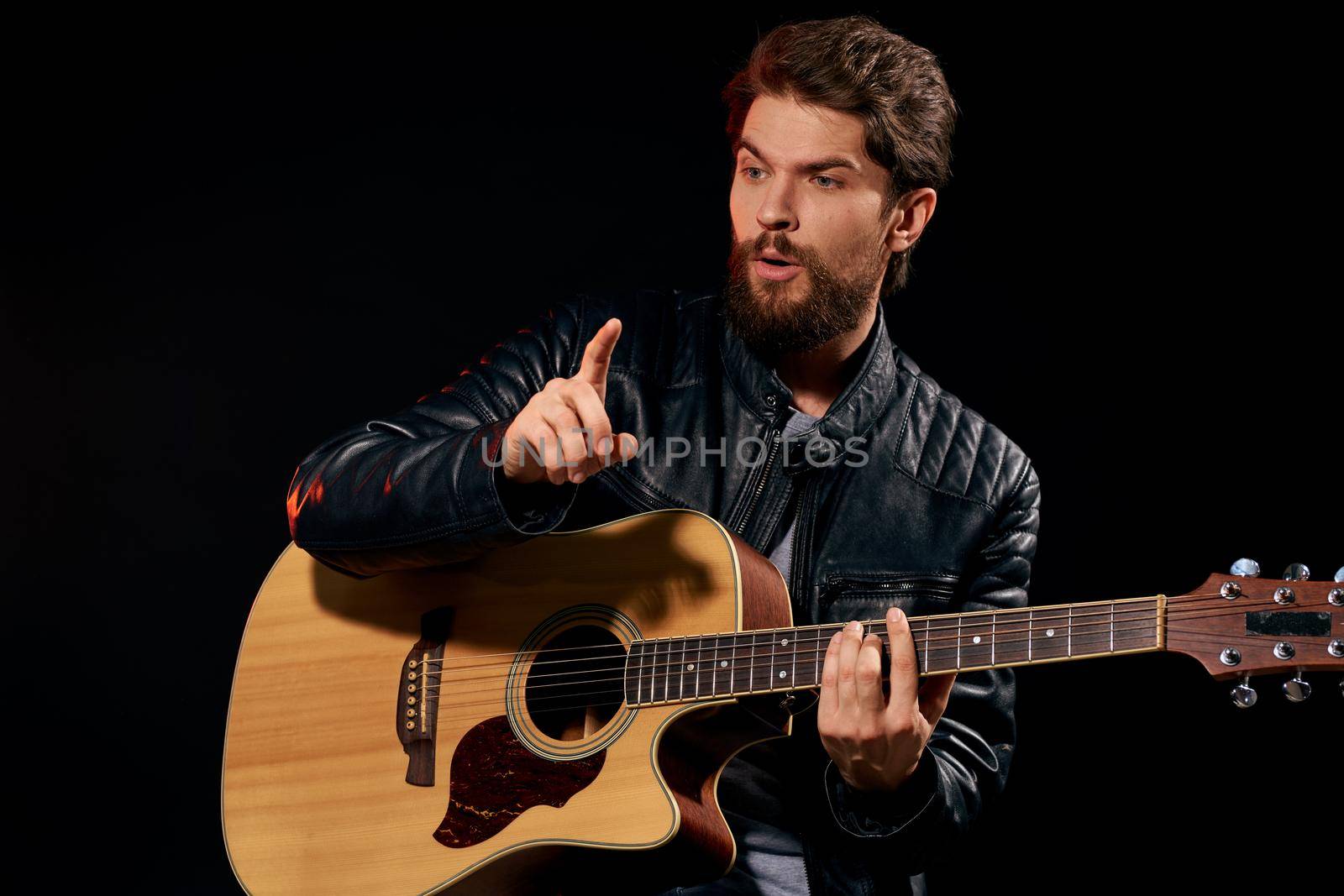 A man with a guitar in his hands leather jacket music performance rock star modern style dark background. High quality photo