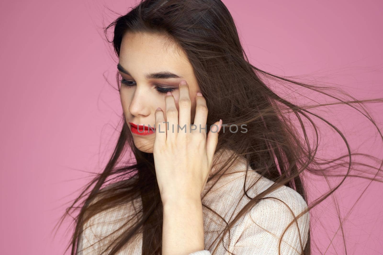 Pretty brunette in a white sweater red lips attractive look pink background. High quality photo