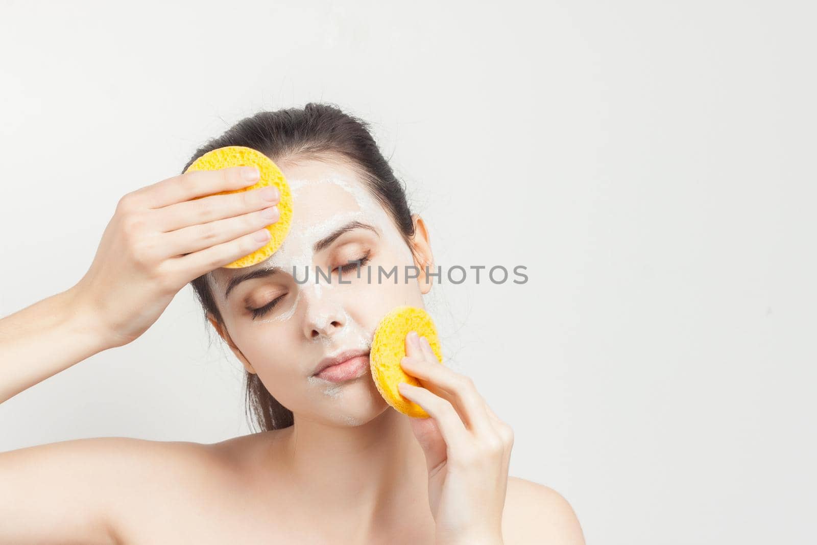 brunette with bare shoulders face mask sponges in hands. High quality photo