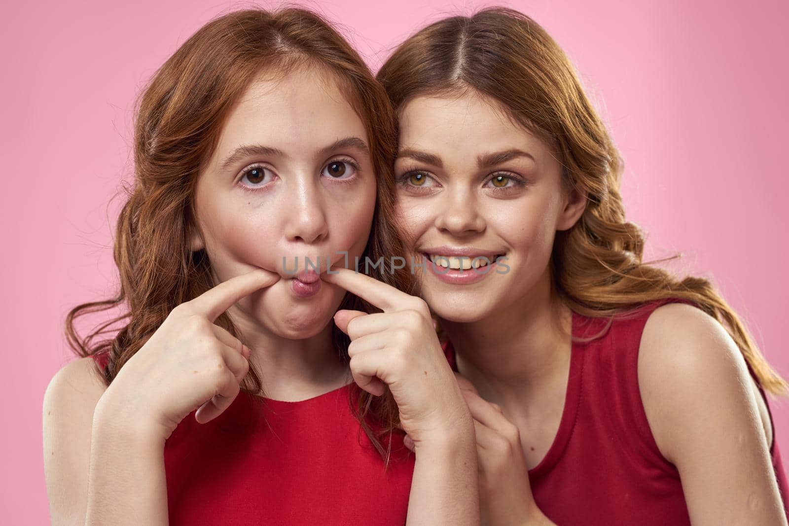 Mom and daughter in red dresses hugs fun grimace childhood joy pink background. High quality photo