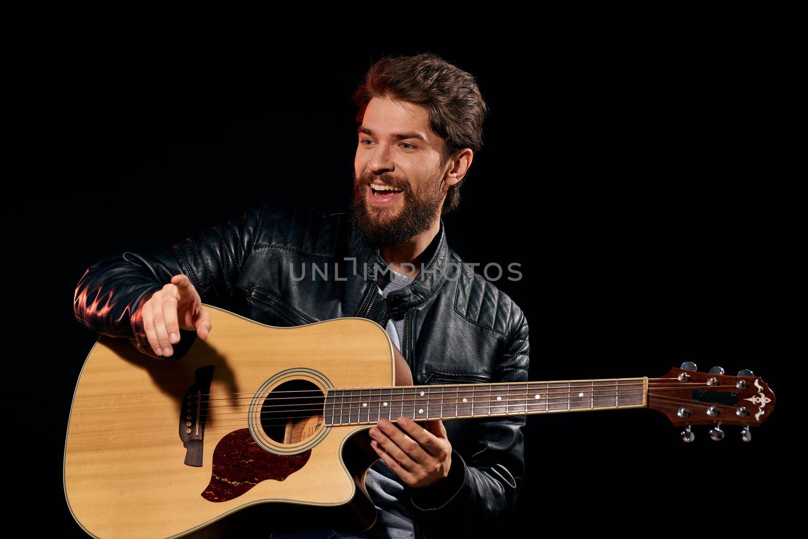 A man with a guitar in his hands leather jacket music performance rock star modern style dark background. High quality photo