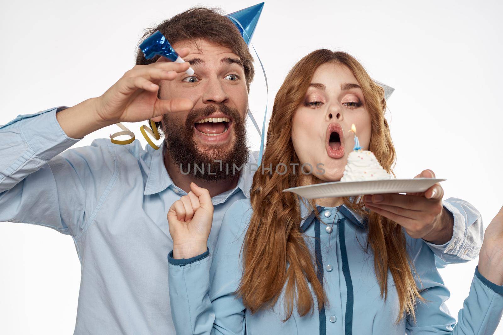 energetic man and woman with a cake and in hats celebrate a birthday on a light background. High quality photo