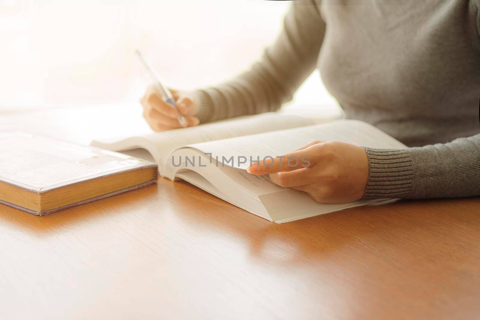 Close-up Asia woman writing paper at the desk with pen and reading books at table with at library university. Self-education concept by thanumporn