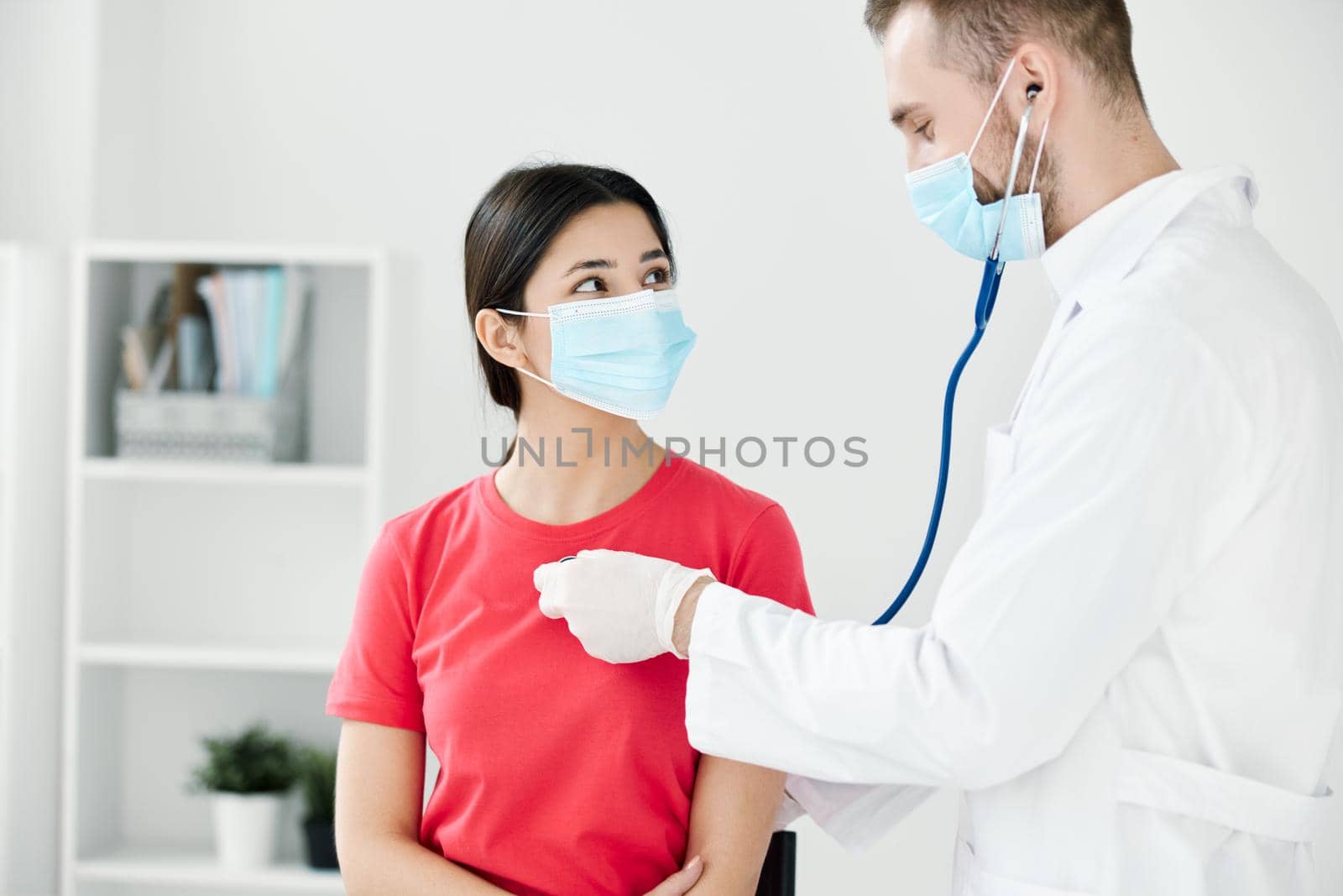 doctor in a medical mask and a dressing gown examine a woman in a t-shirt at the hospital by SHOTPRIME